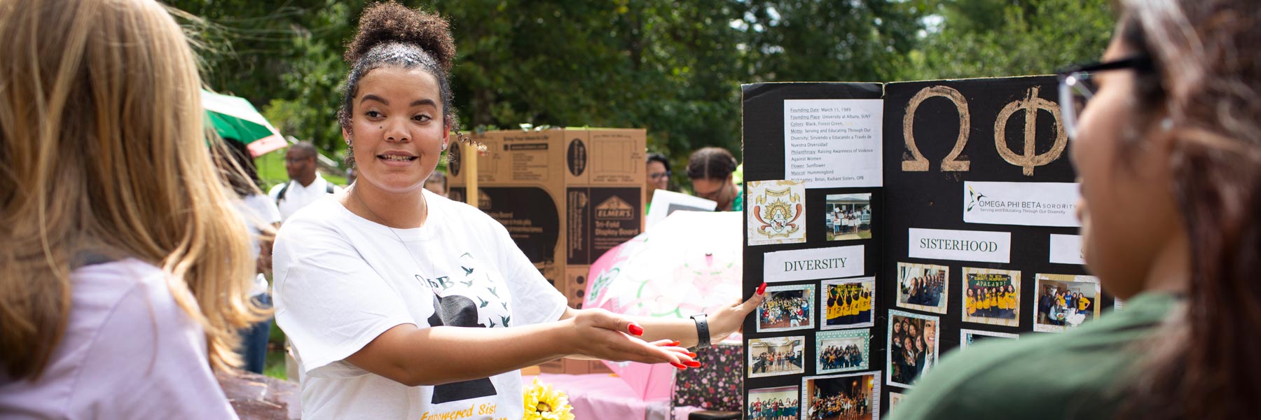 a woman standing in front of a trifold with information about fraternities and sororities